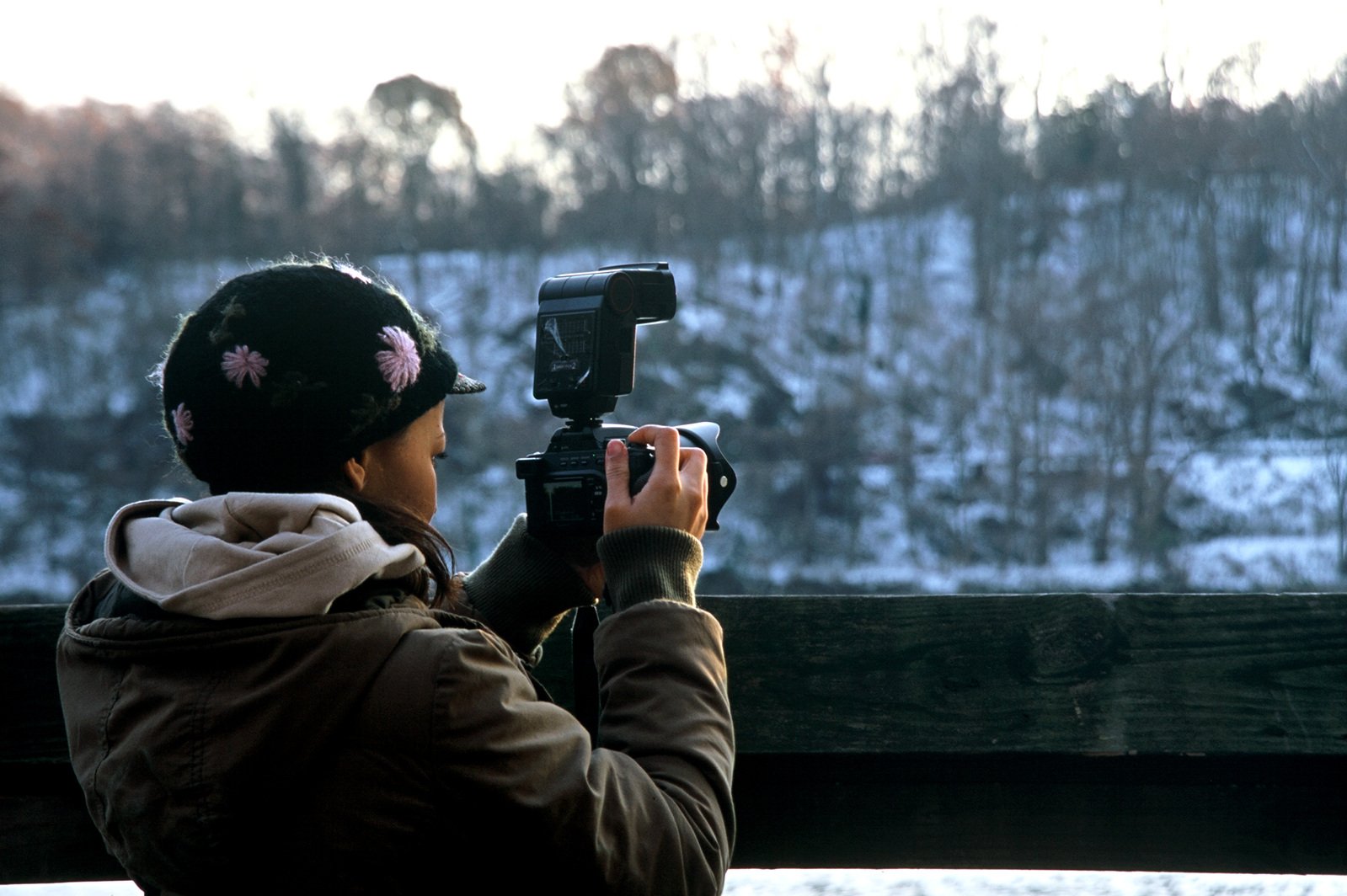 woman taking po with camera on railing of snowy countryside