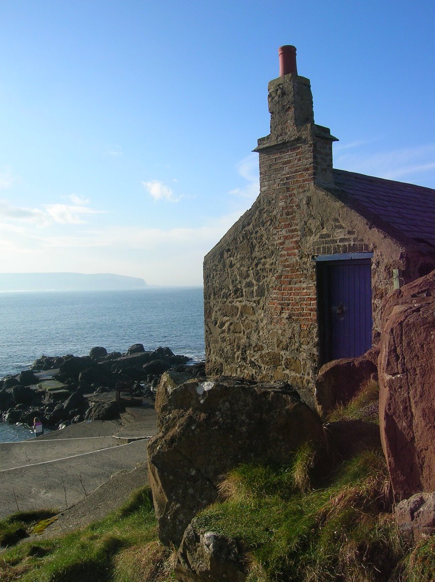 a small building near the ocean and grassy area