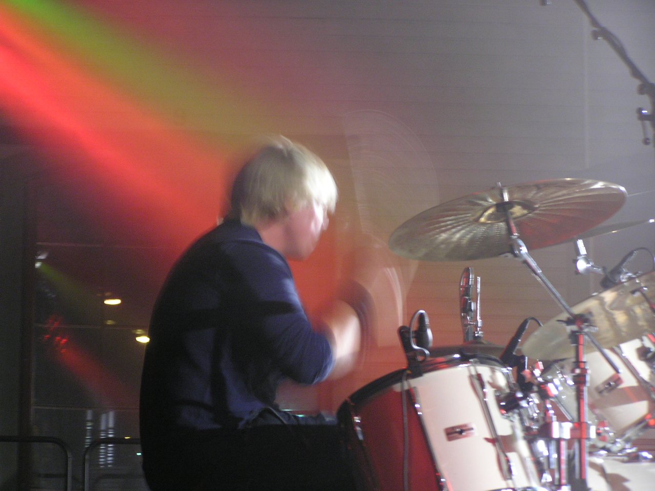 drummer in front of his drum set in front of a red and green light