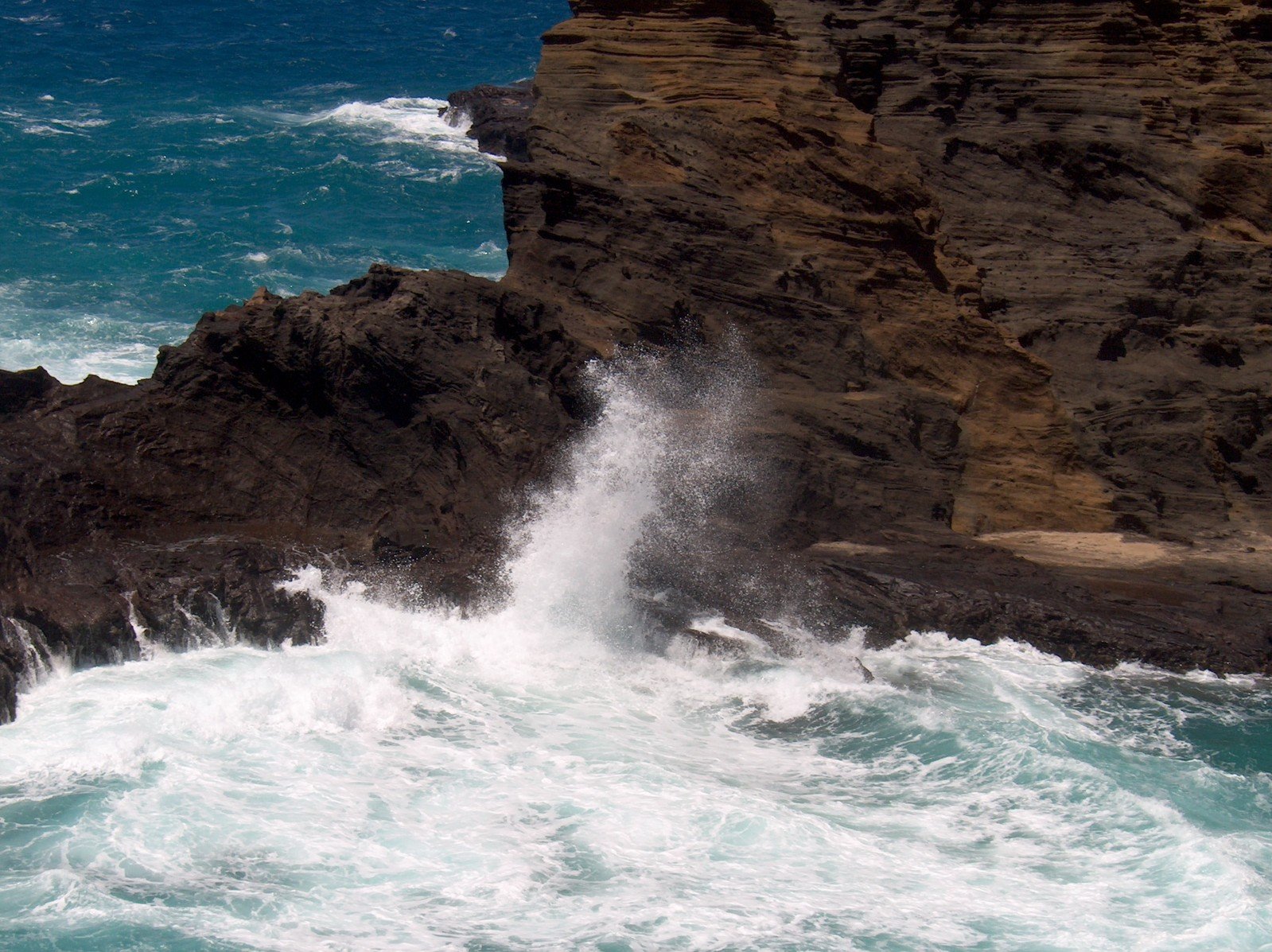 the waves are breaking off the rocks by the cliff