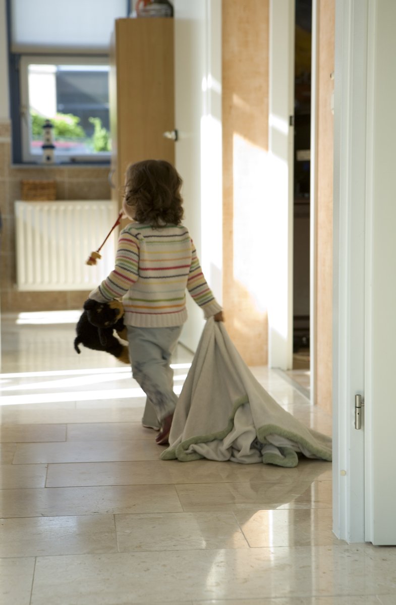 a toddler wearing a sweater carries a teddy bear through the room