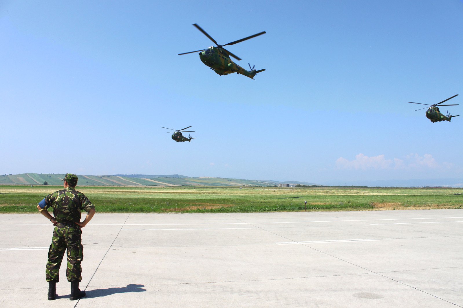 a soldier in camouflage watches four helicopters in the sky