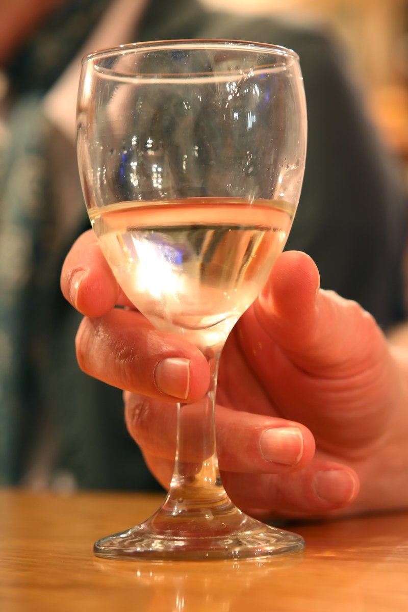 someone holding a glass of white wine at a restaurant