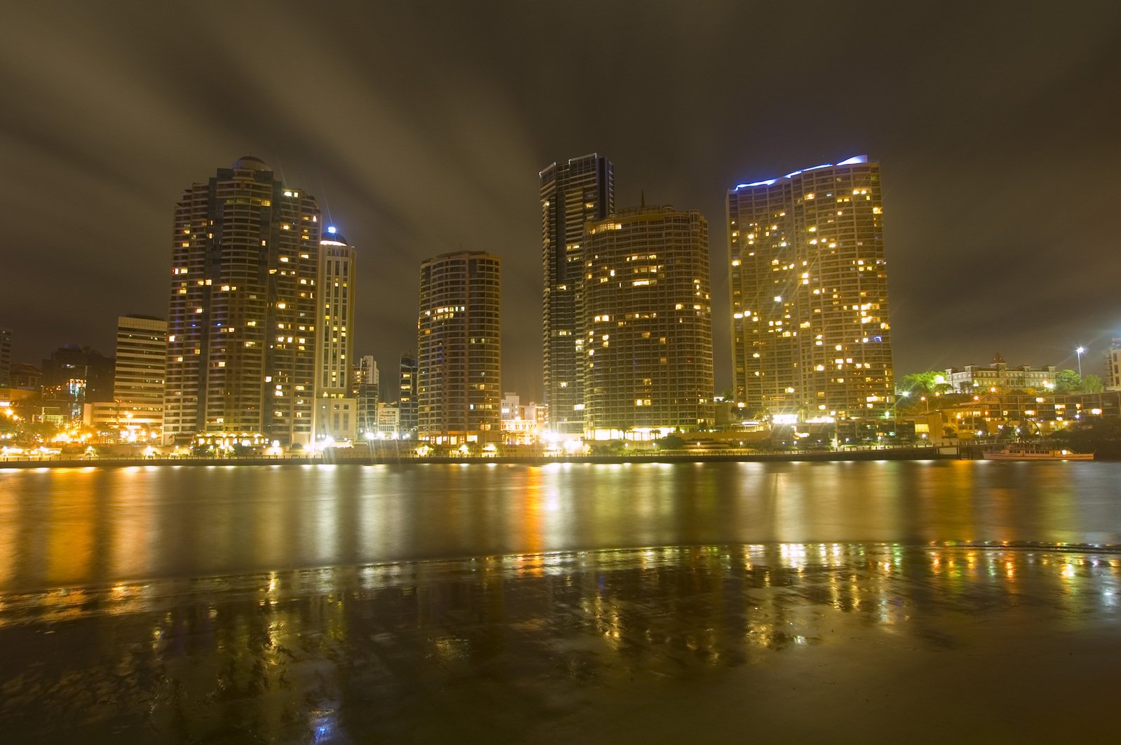 several tall buildings lit up in the night by water