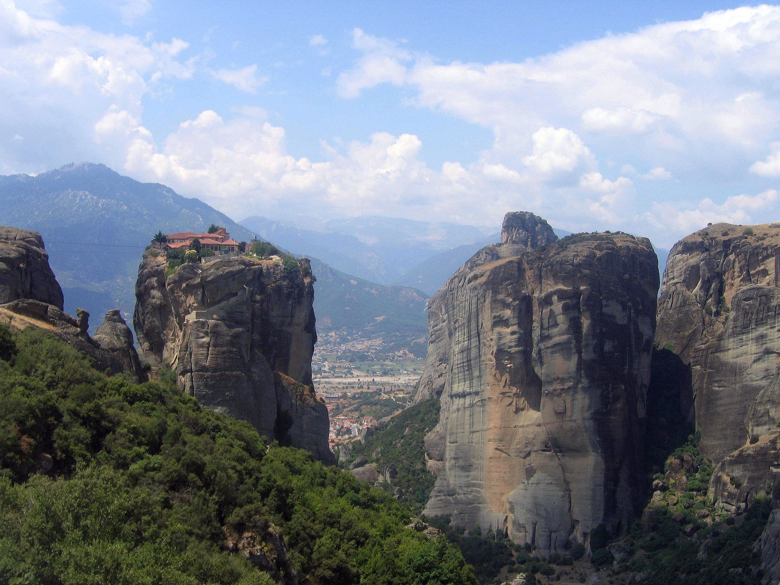 a beautiful rocky landscape shows towering mountains and houses, while blue skies dot the distant sky