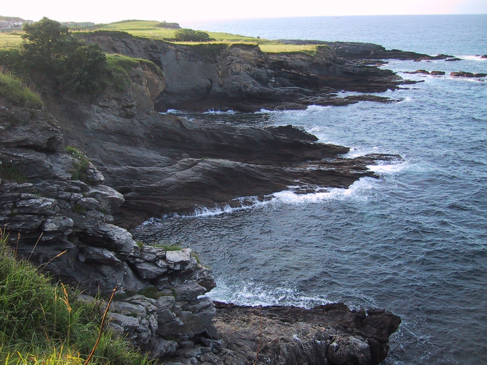 a man in red jacket and sunglasses sitting on rocks overlooking water