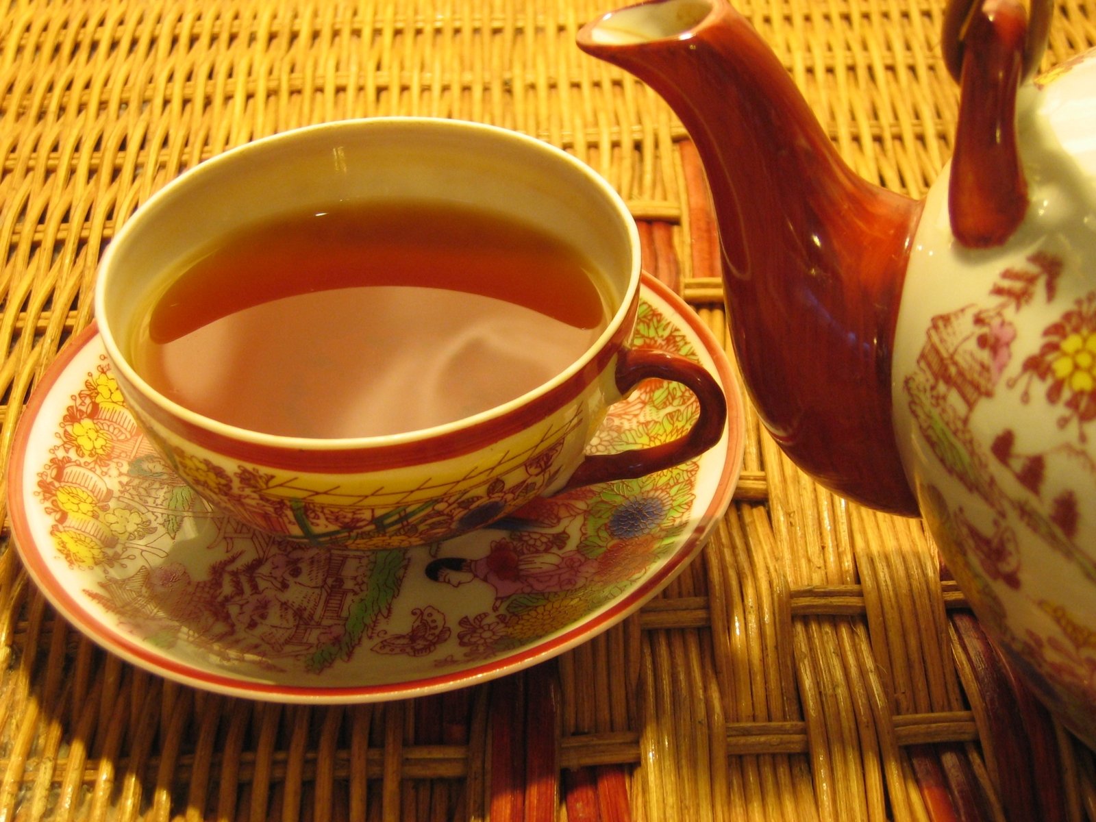 a red and yellow tea cup and saucer next to a white teapot