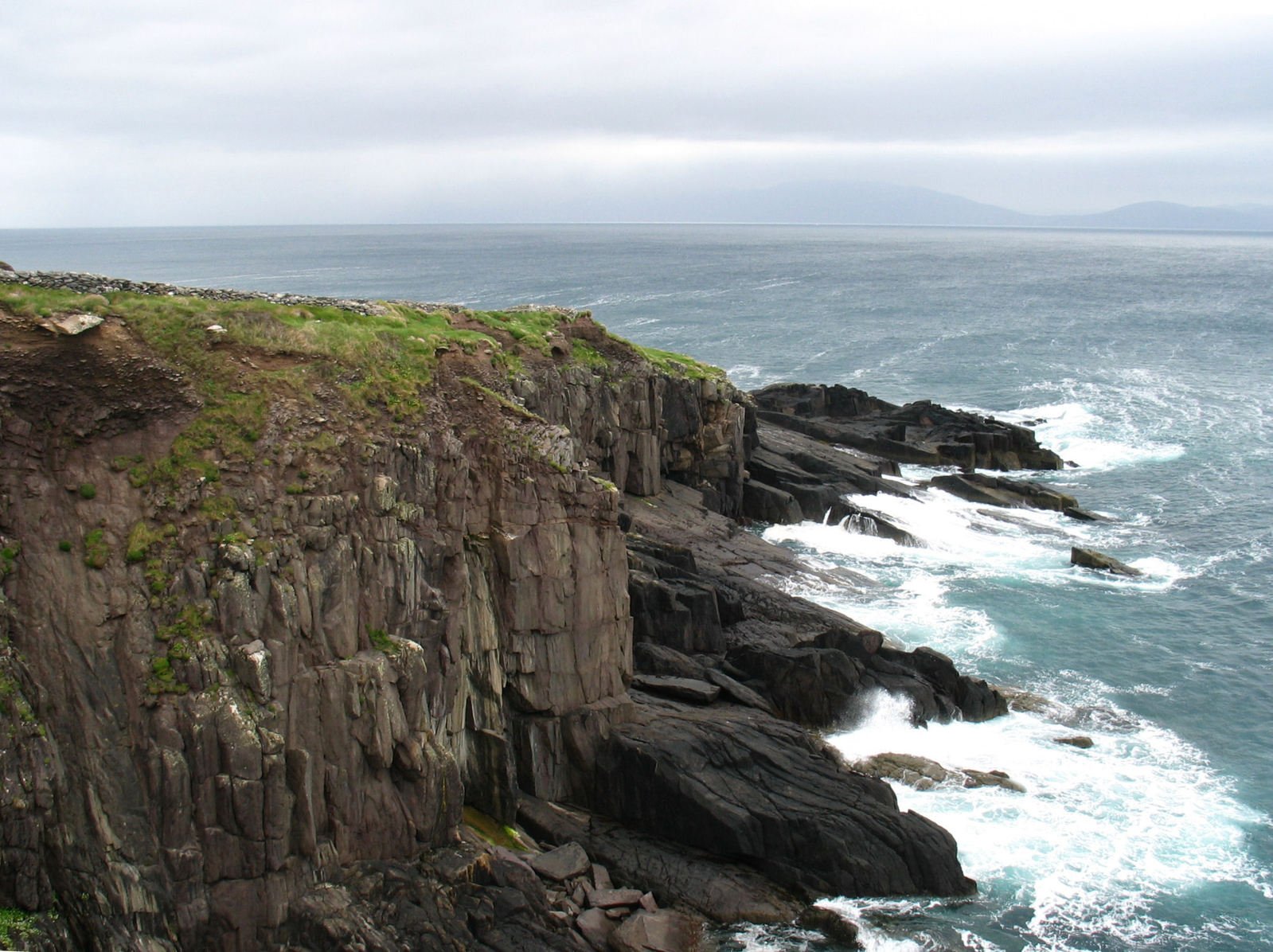 the ocean is next to an cliff with a grass and rocks edge