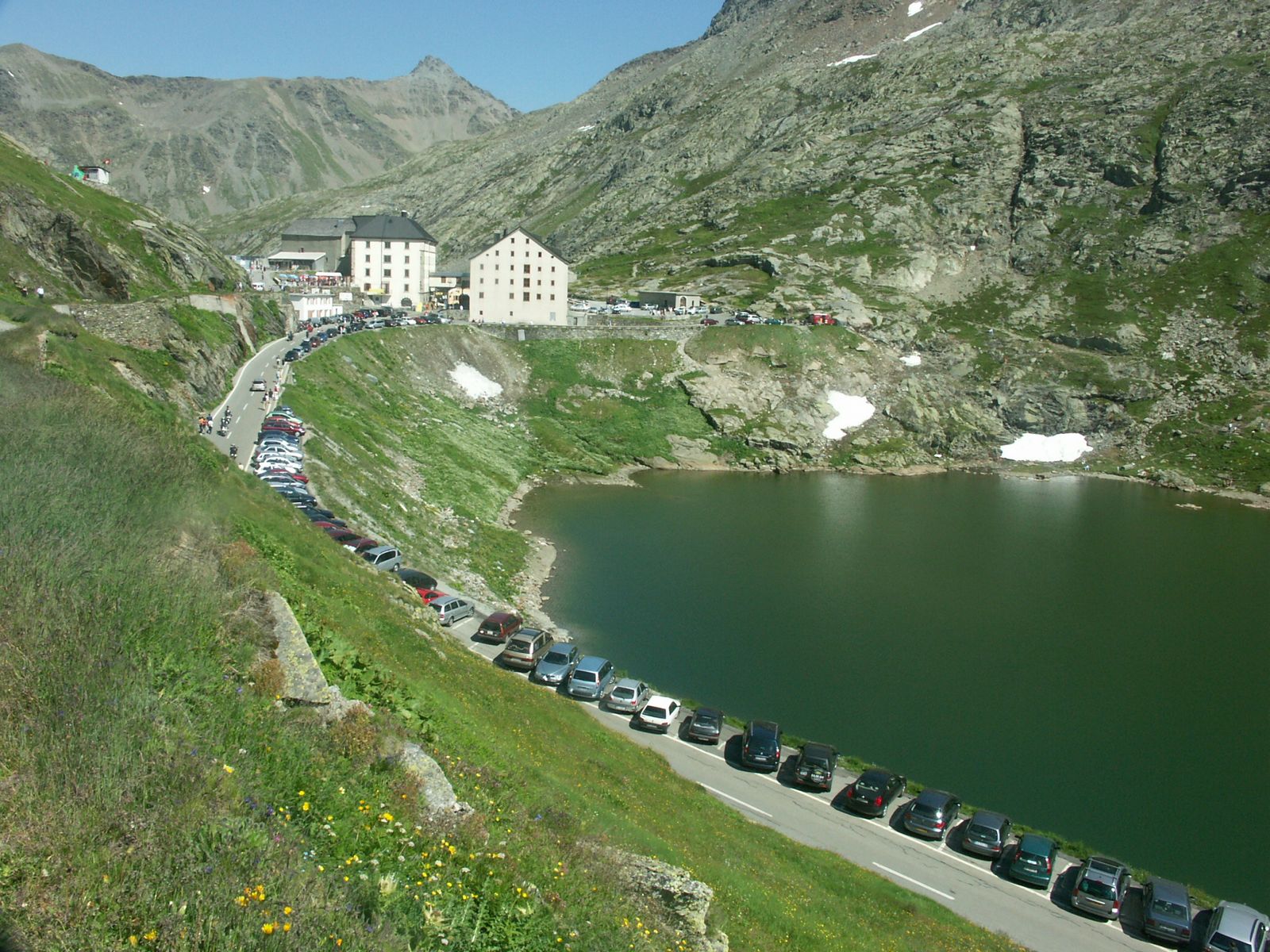 a bunch of cars parked on a hill in front of a large lake