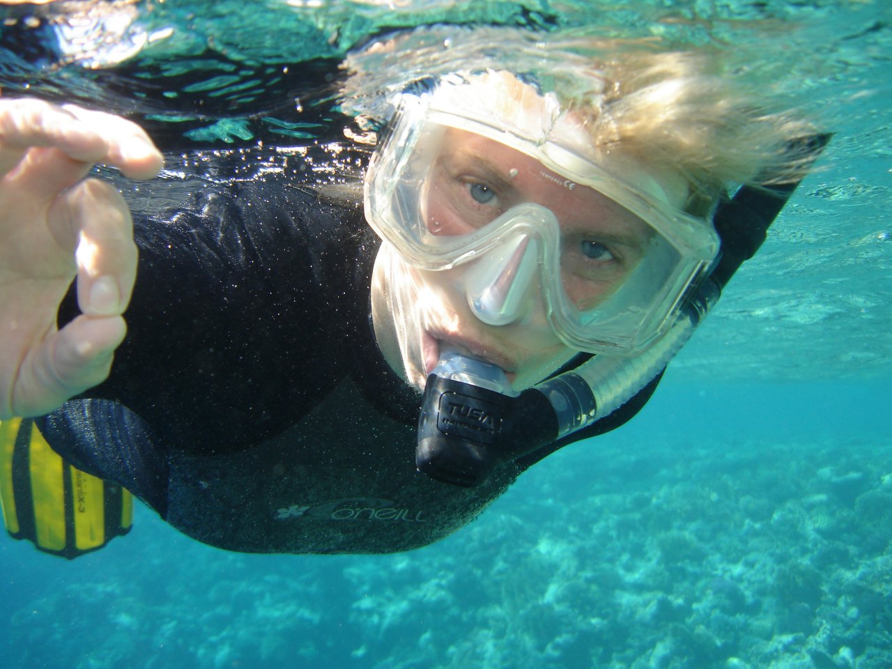 man in diving gear holding soing up while wearing goggles