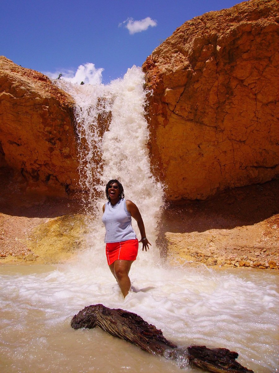 a woman in red shorts standing under a waterfall