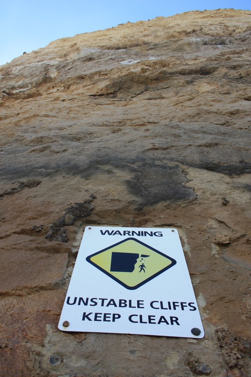 an unattable cliffs keep clear sign attached to a large rock wall