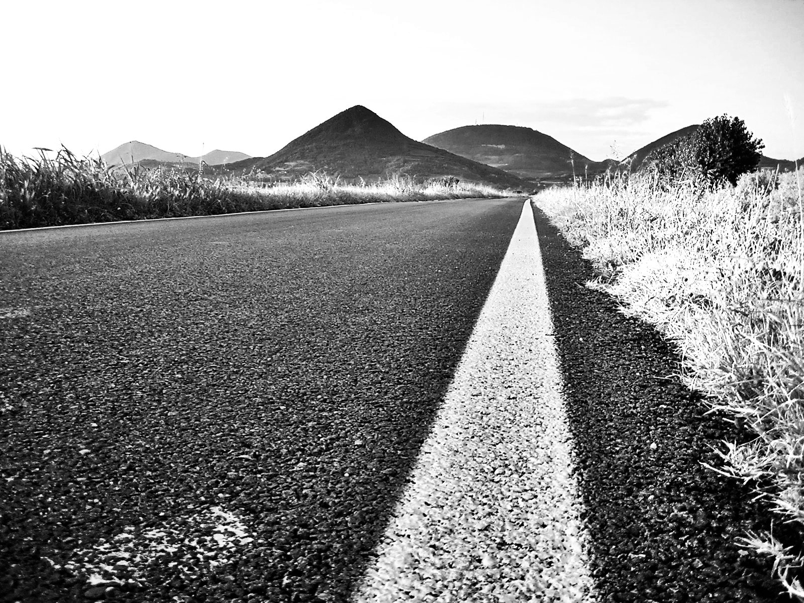 an empty road leading to mountains under a cloudy sky