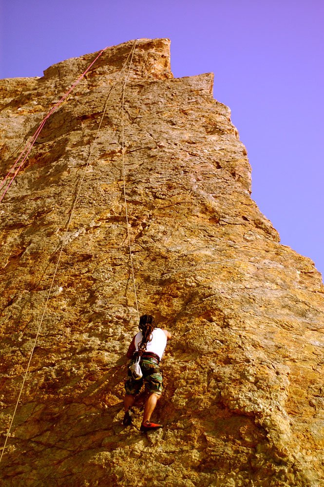 man climbs up the side of a cliff in the sun