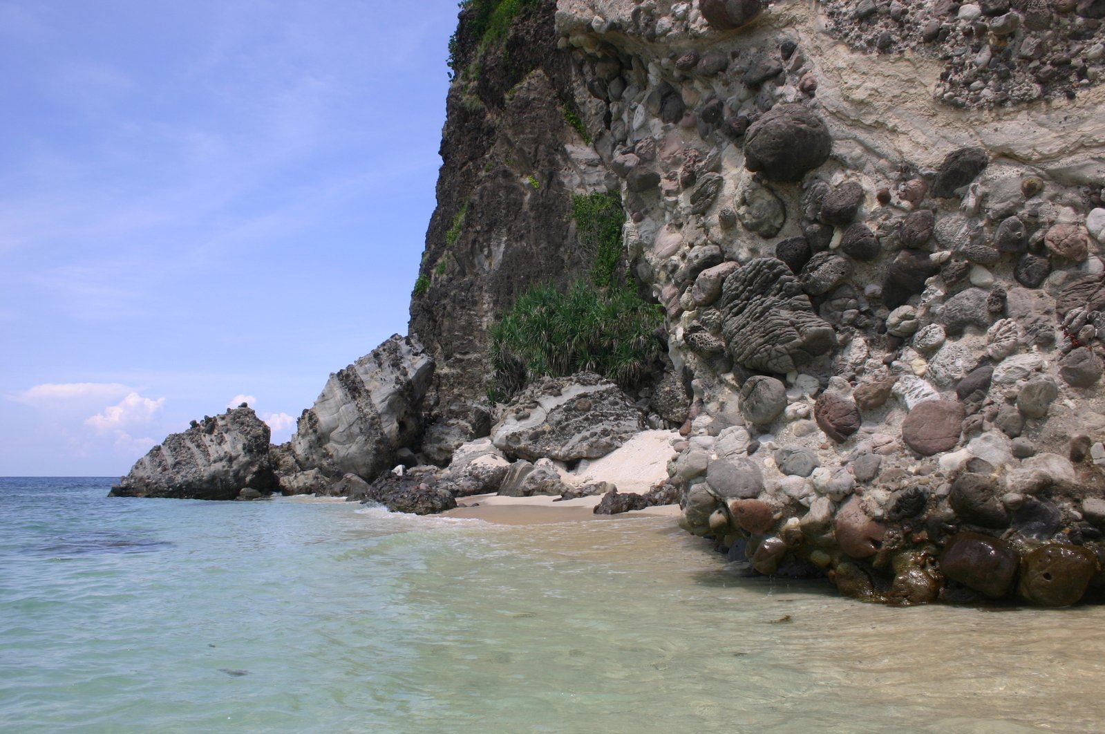 a beach with several large rocks by a cliff