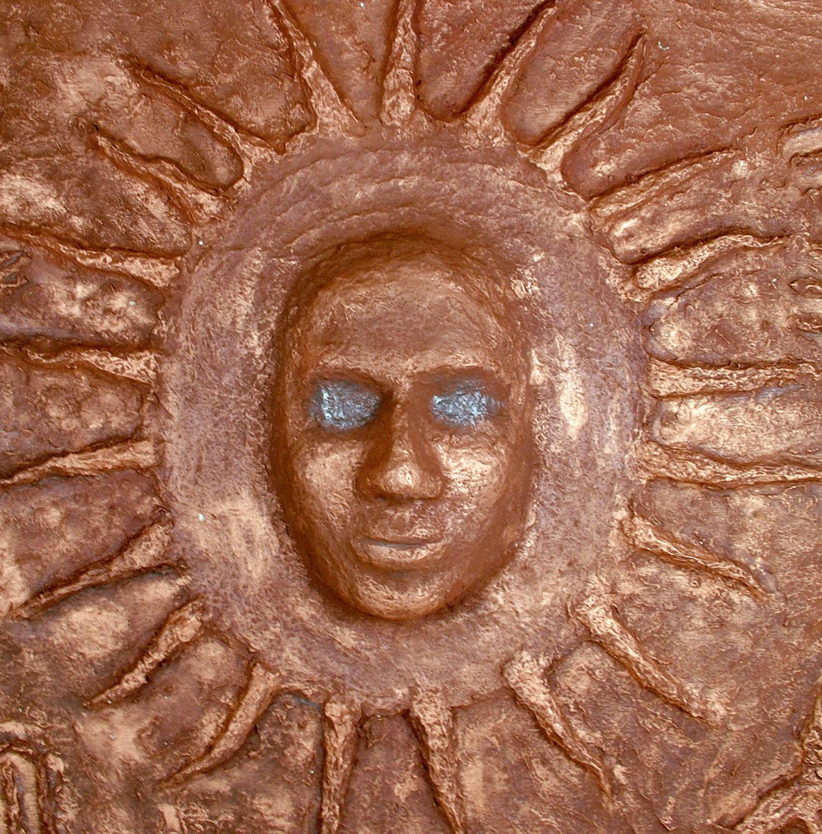 a face made from clay sits in the center of a plaque
