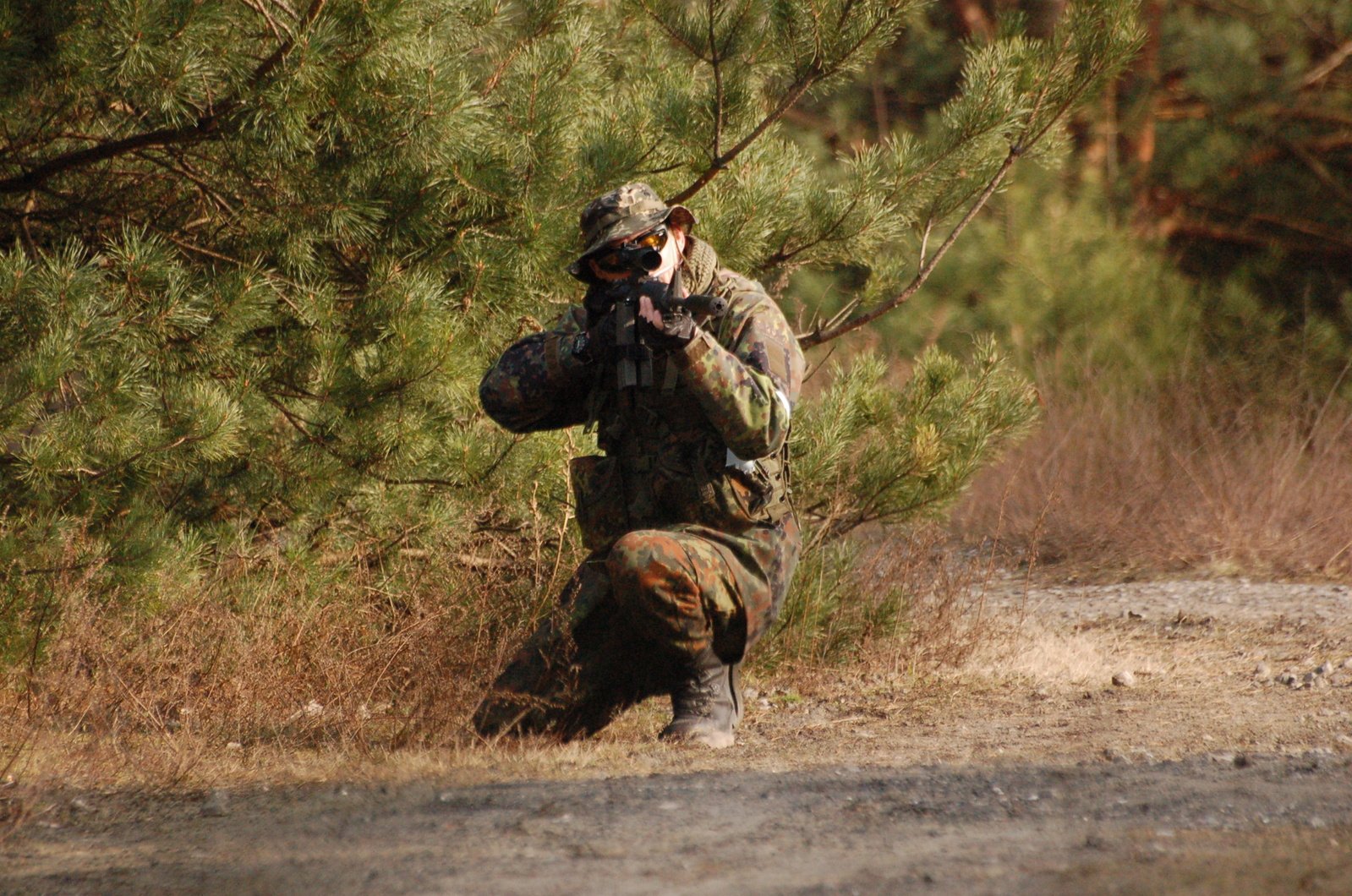 a man in camouflage is standing by a tree and holding a gun