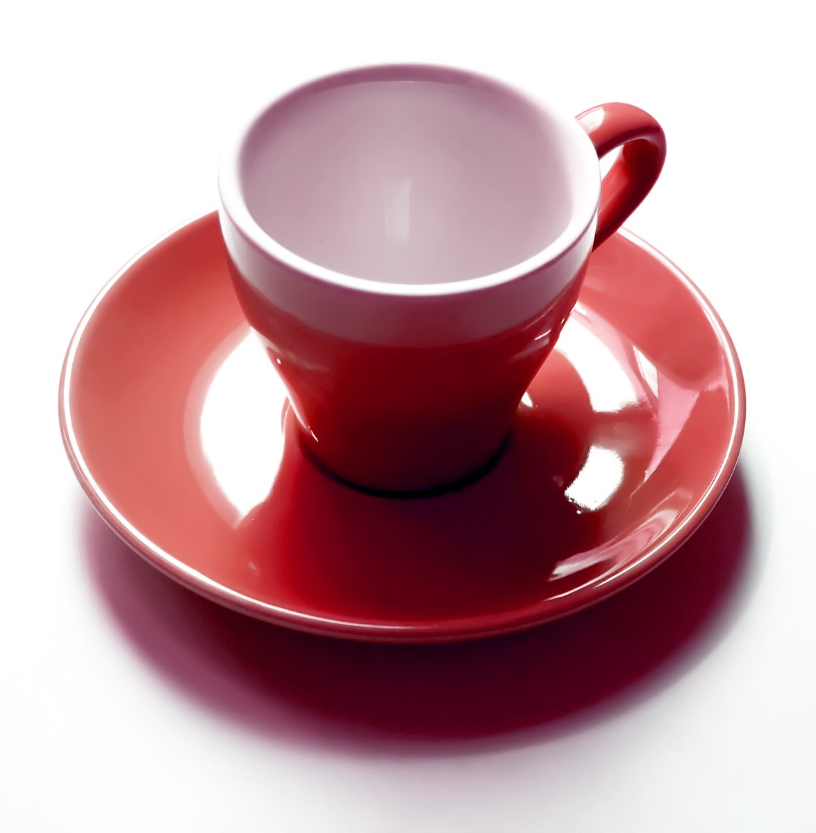 a red cup and saucer sits on a white surface