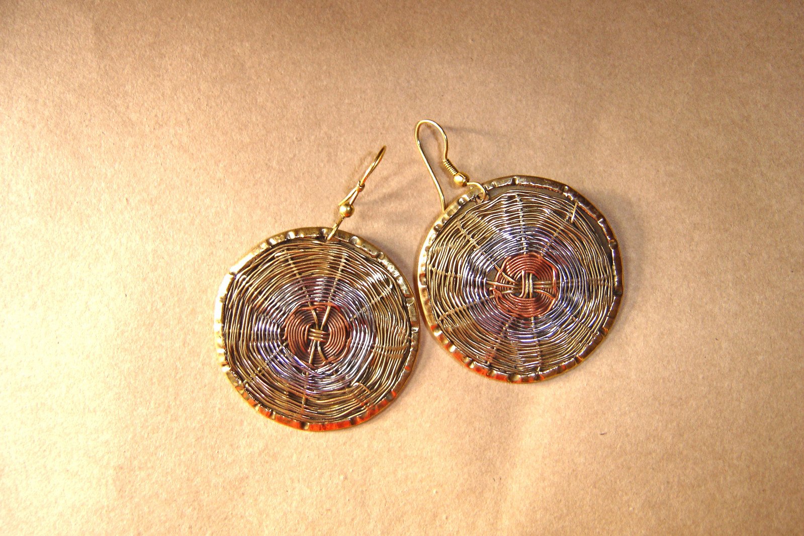 small round metal wire wrapped earrings hanging on a beige background