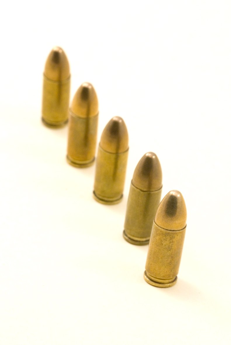 five bullet shells on white surface lined up