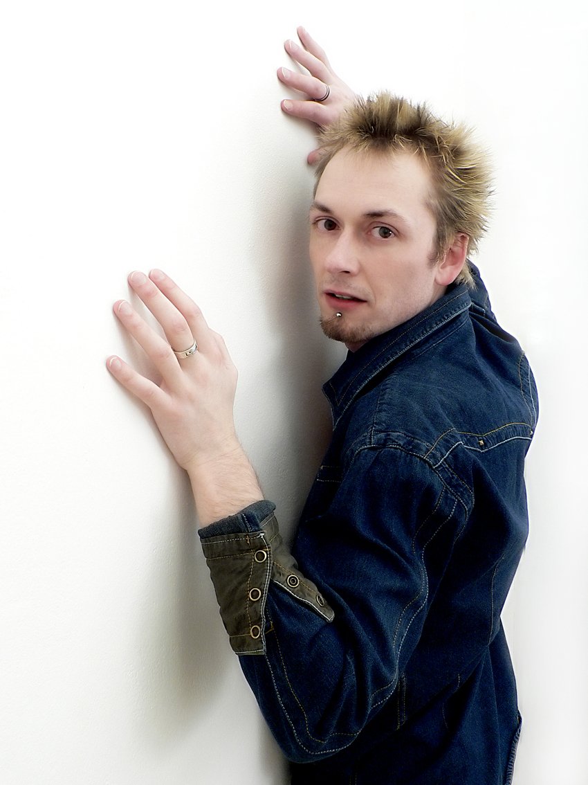 a man leans against a white wall as he shows his hand out