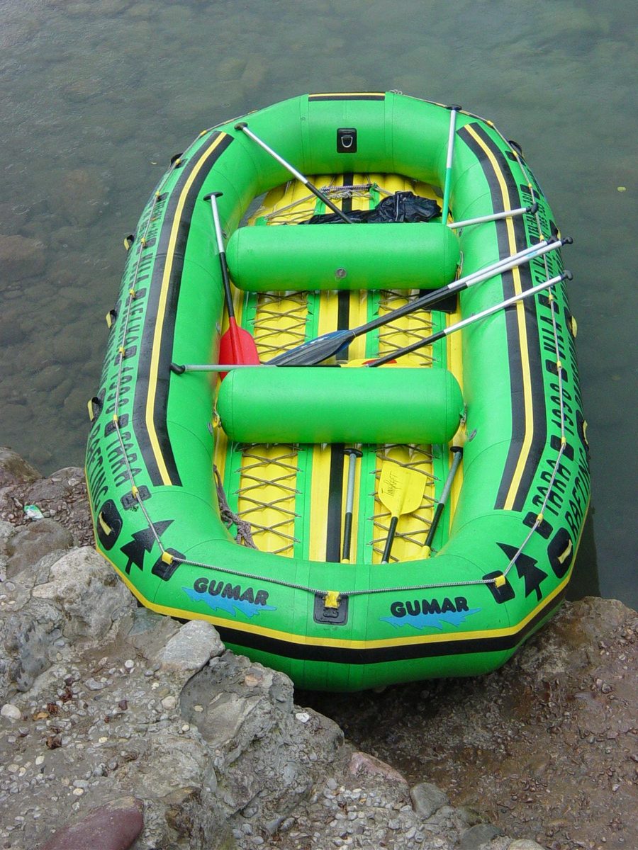 a yellow and green inflatable raft tied to a rock near water