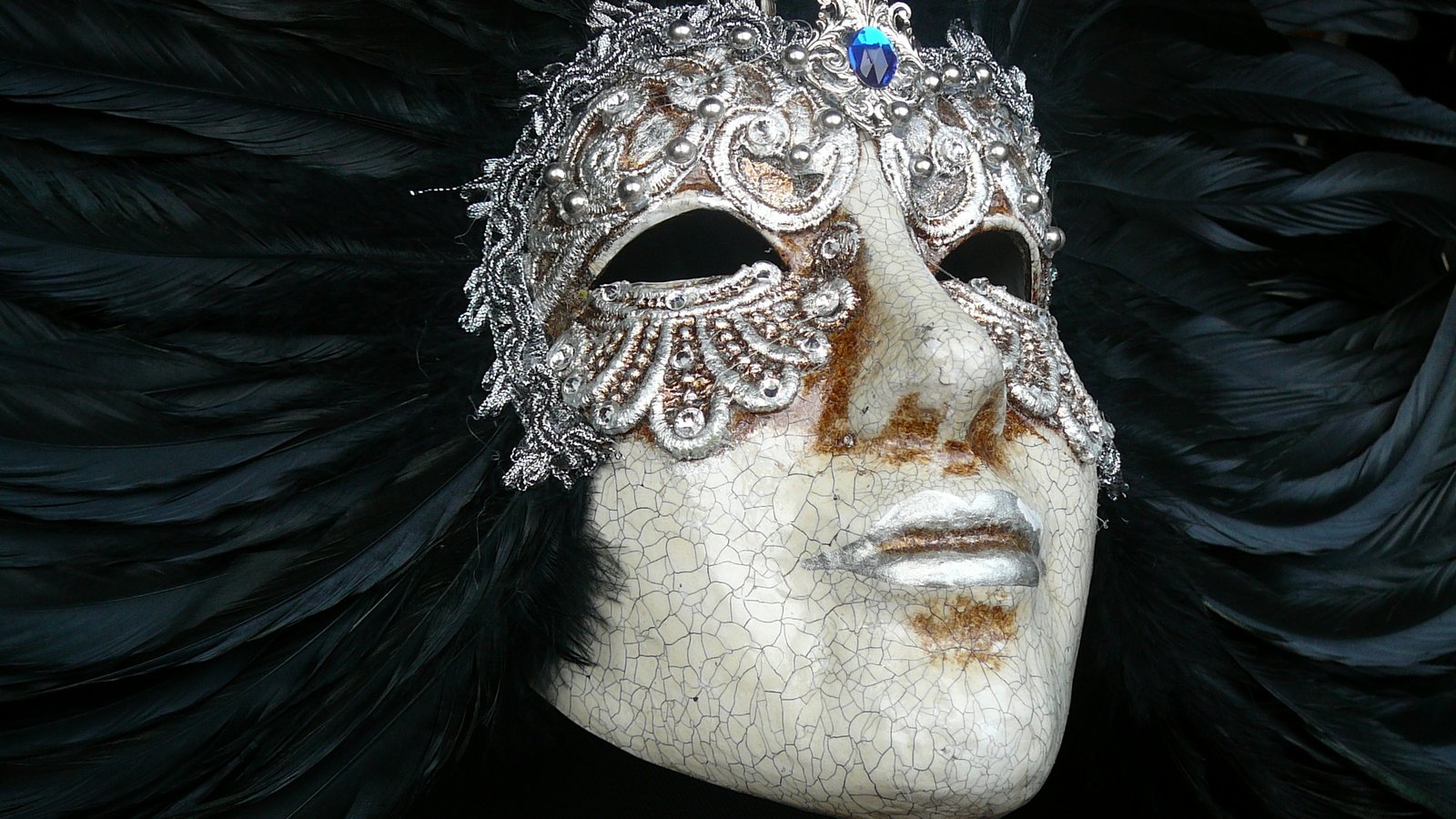 a mask with feather in its eyes on a dark surface