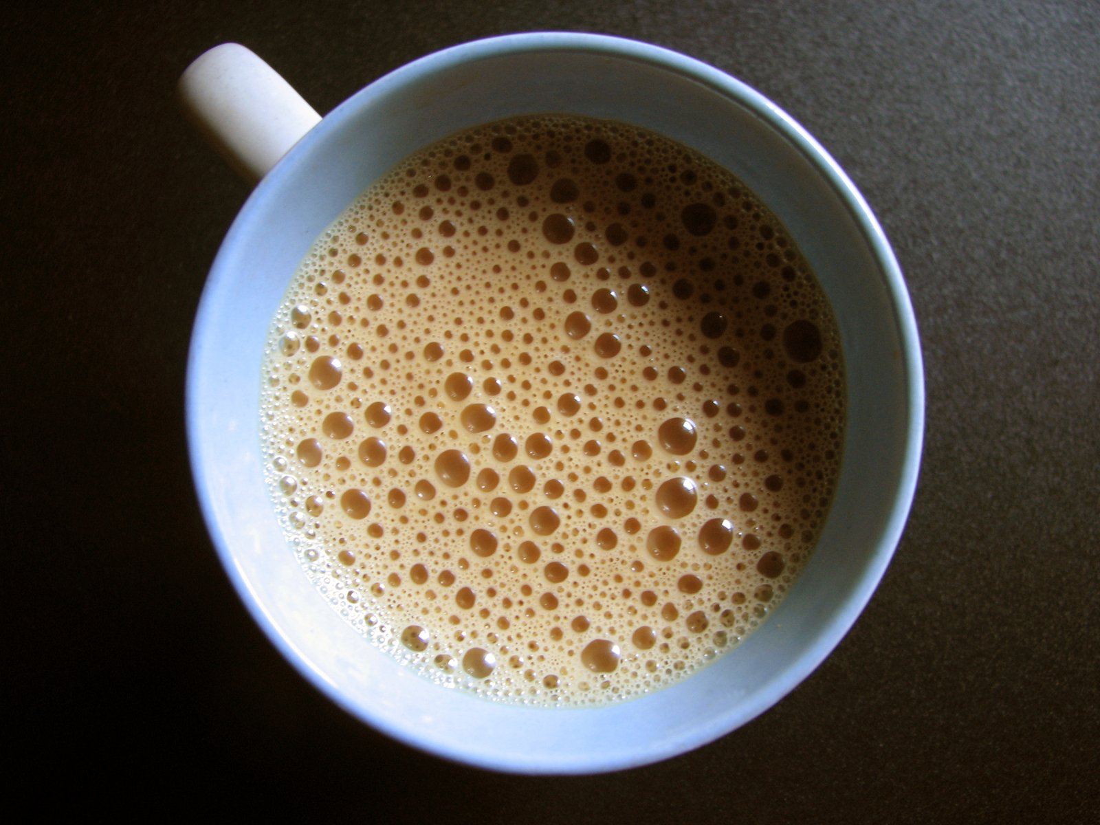 a cup of white coffee is sitting on a dark surface