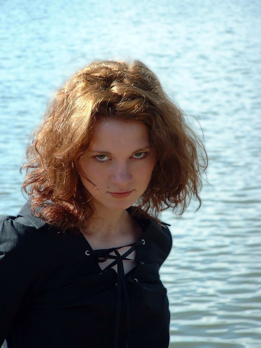 a woman with hair and big eyes standing near the water