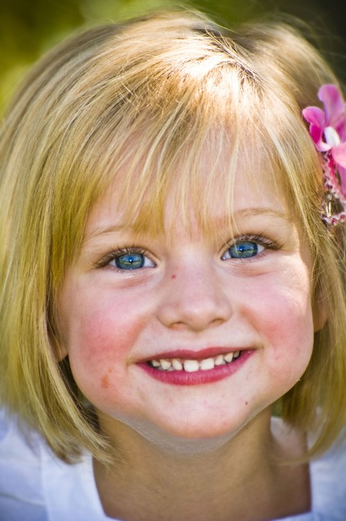 young blonde girl with blue eyes and a pink flower in her hair