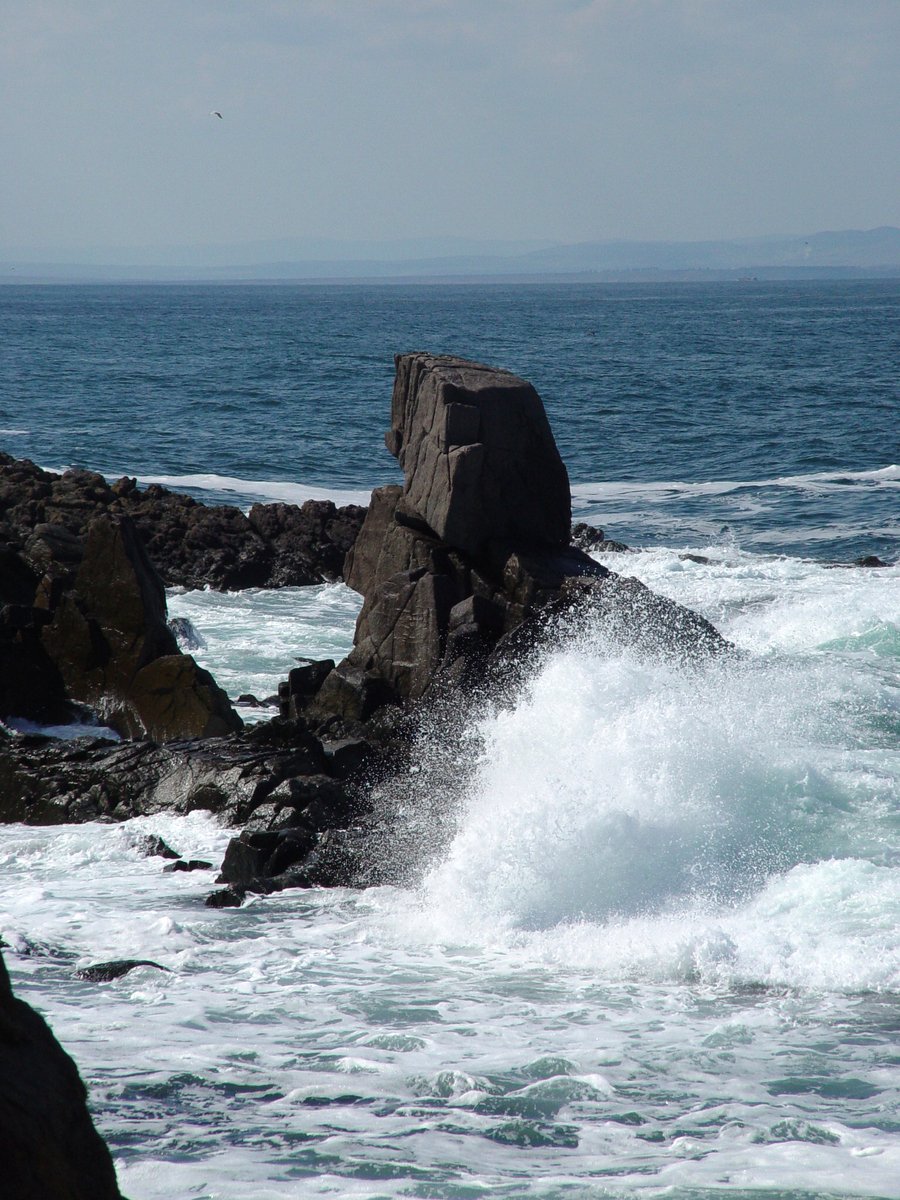 a rock outcropping into the ocean, with crashing waves in front of it