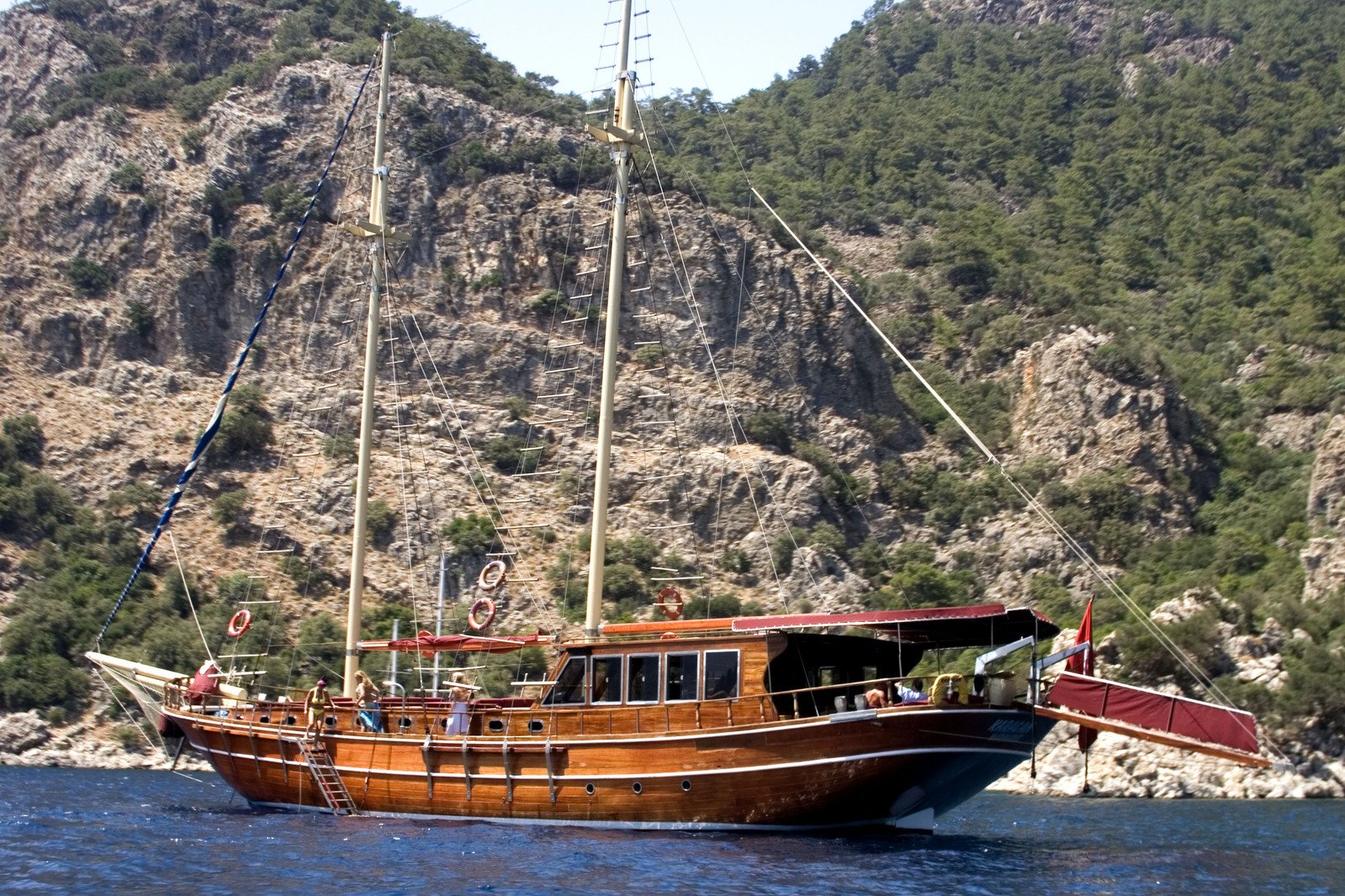 a brown sailboat sailing on a body of water near a mountain