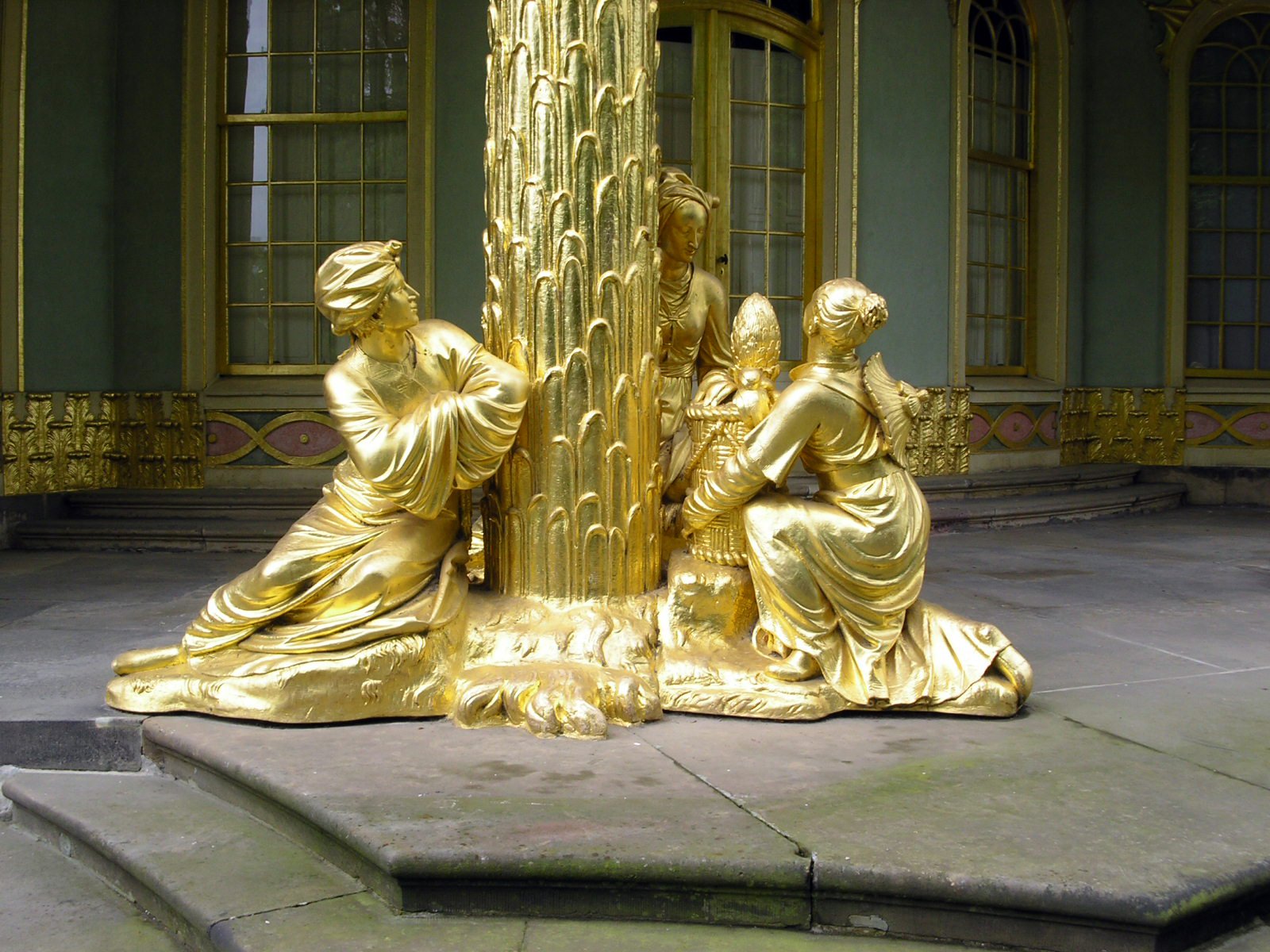 a gold colored sculpture of women, a man and a woman at the base of a gold pillar