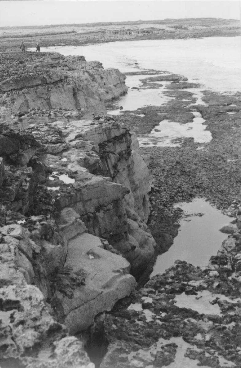 a small man standing on the edge of some rocks looking over the water