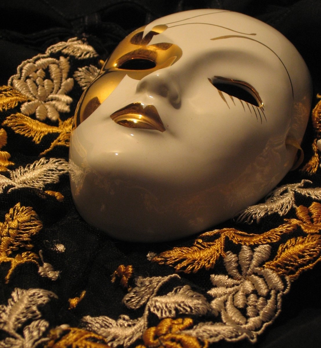 a white mask with gold eyes sits on a gold fabric