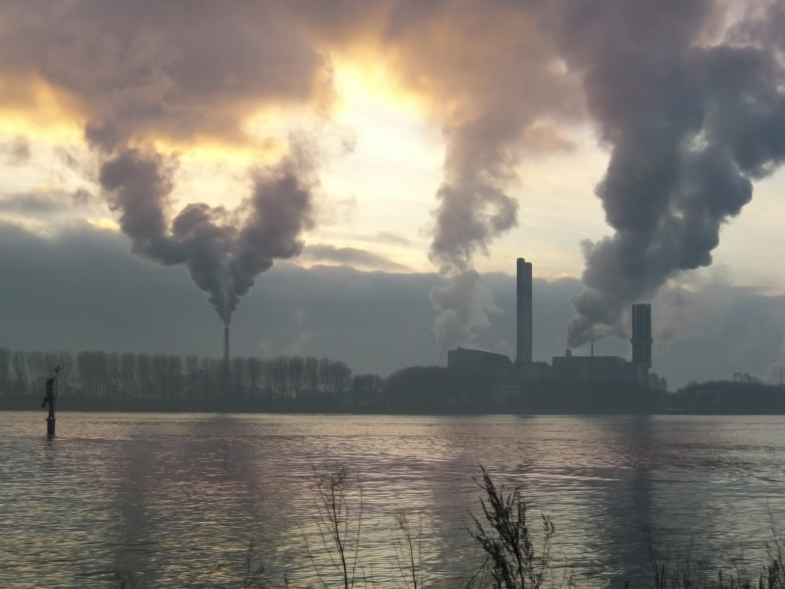 smokestacks billowing from industrial factories by the water