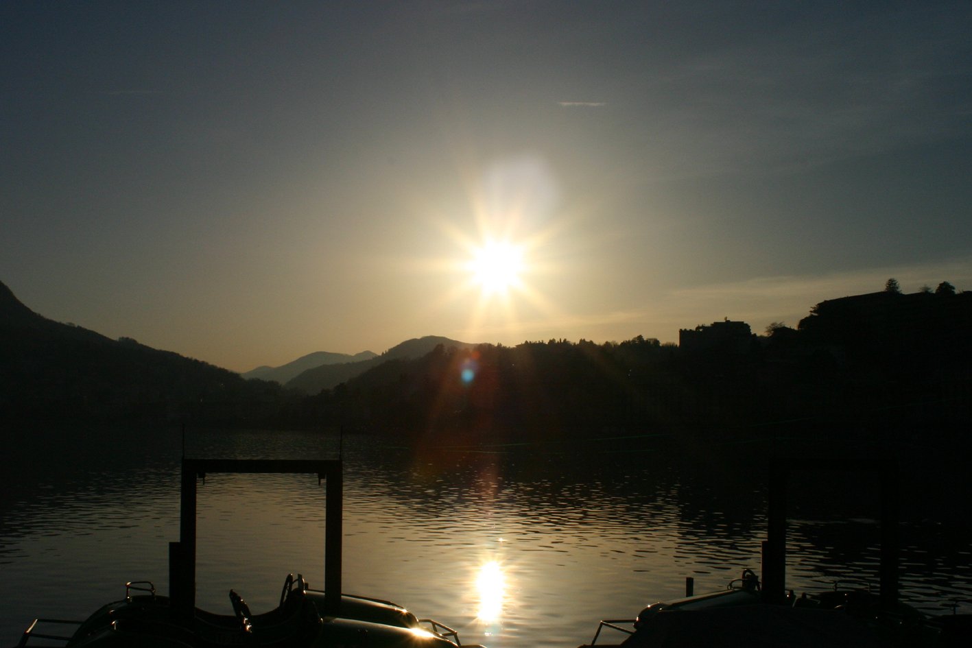 the sun rises over mountains behind a lake