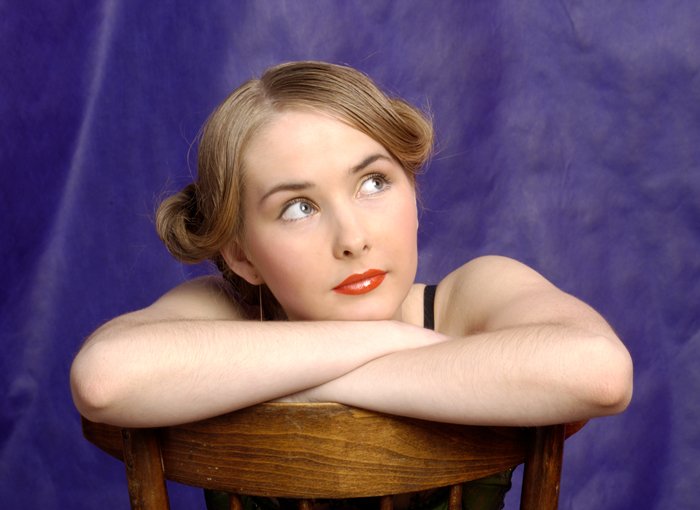 a girl sitting on a chair with her arms over her head