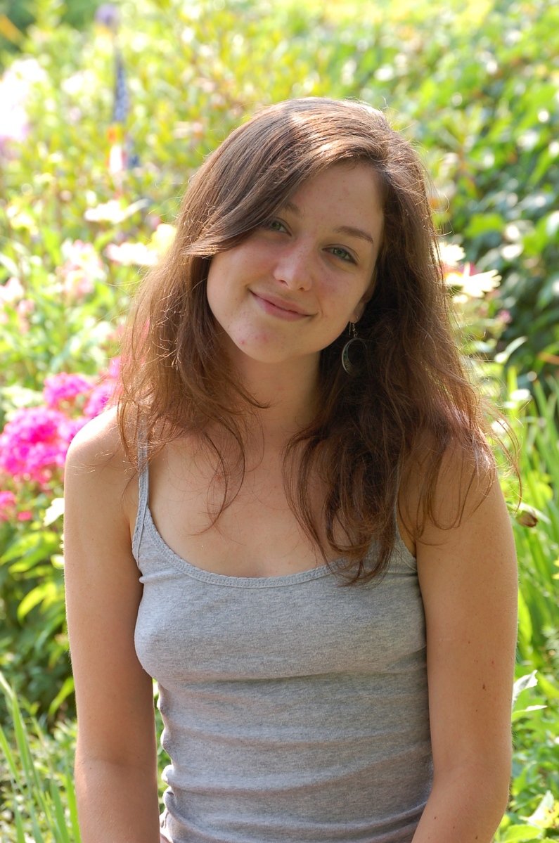 a smiling girl sitting on the ground in front of flowers