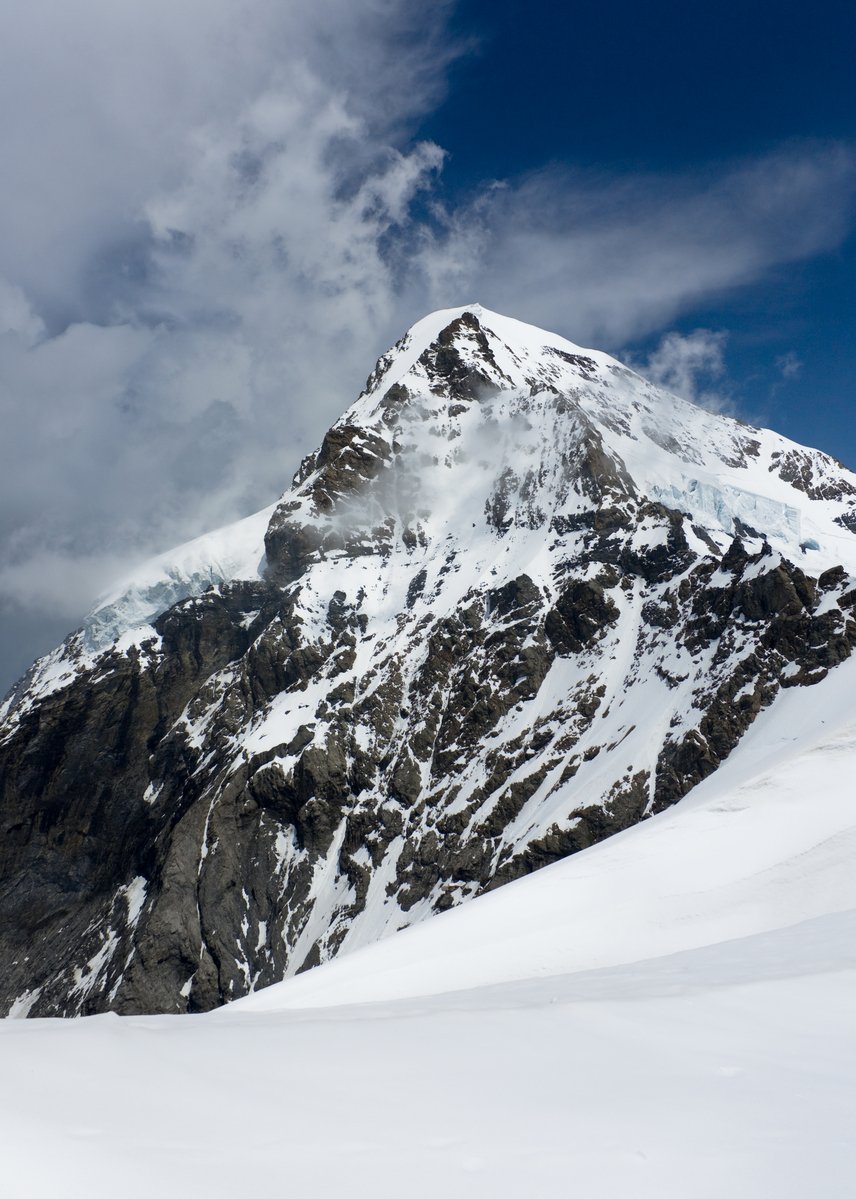 a large mountain covered in snow under a cloudy blue sky