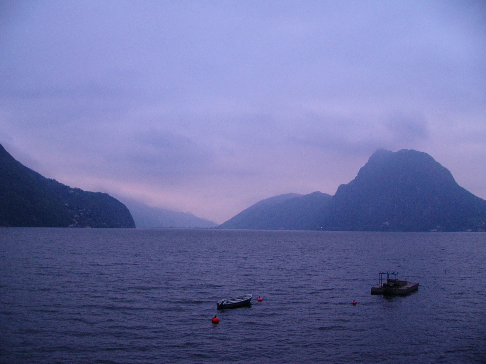 two small boats anchored at the shore with a mountain in the distance