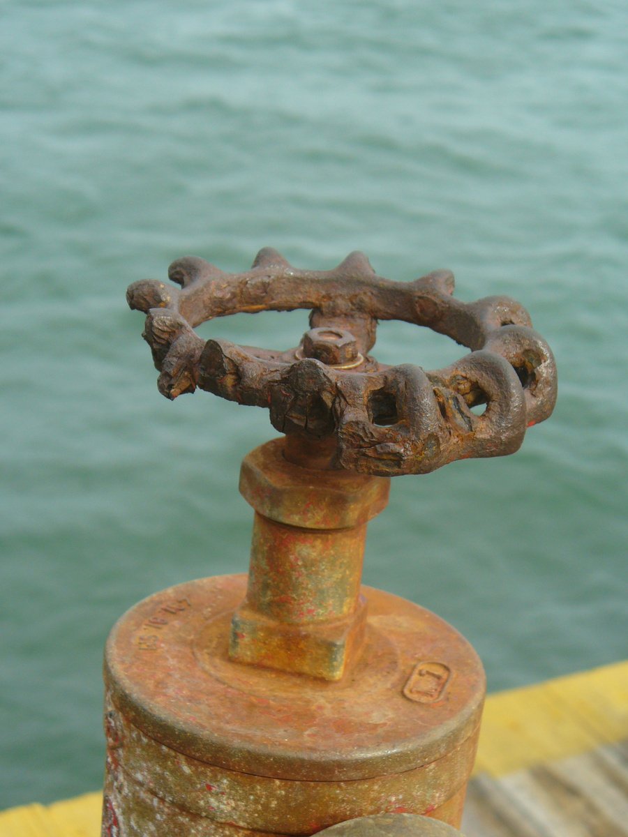 a rusted old spool on the dock near water