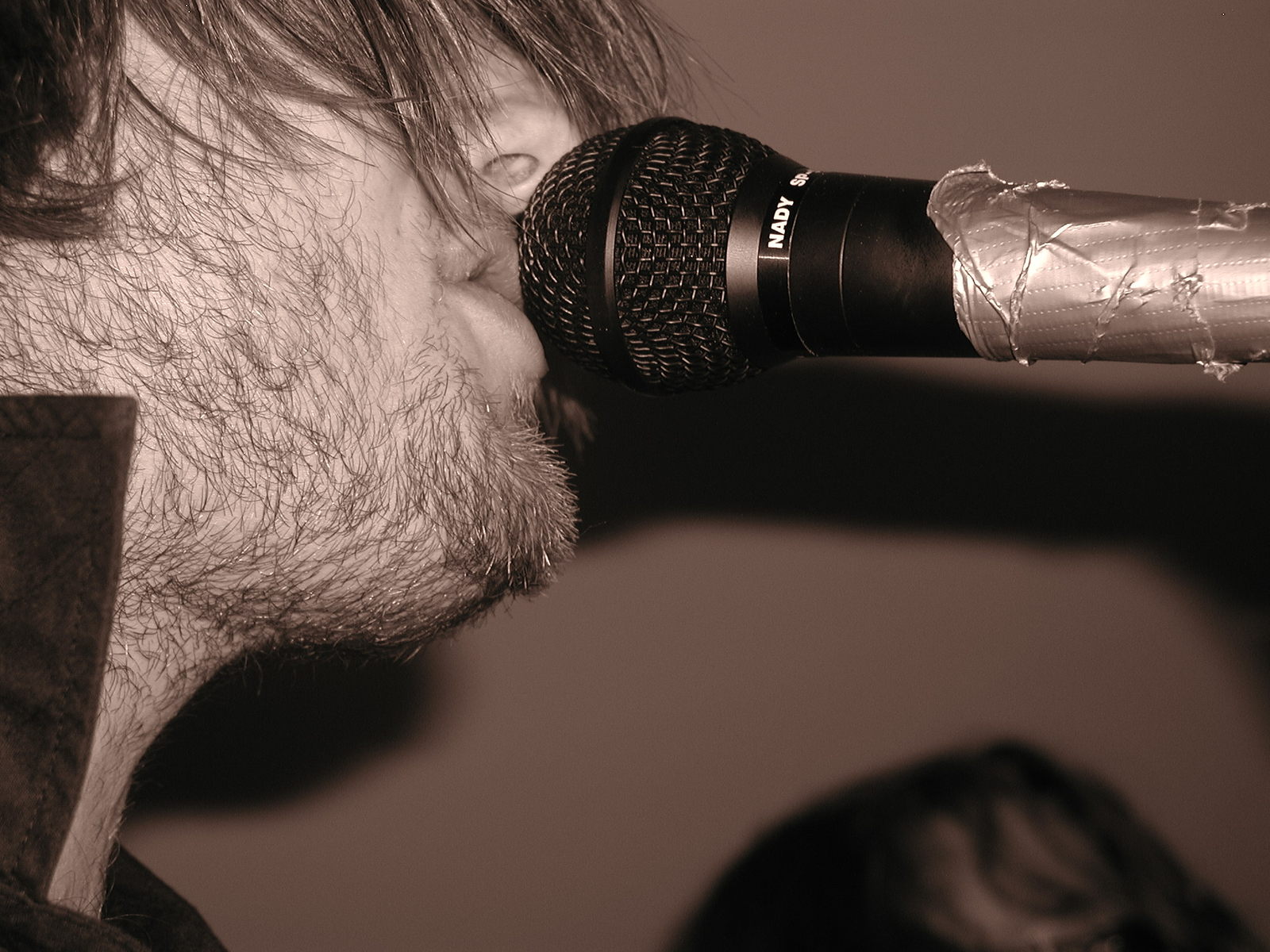 man singing into a large microphone with a silver tube hanging from it's handle