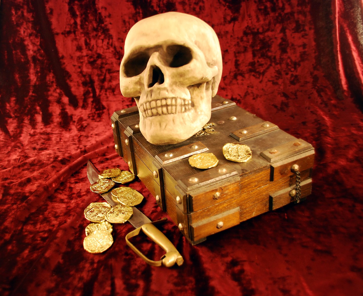 a skull in the top of an old trunk with many coins next to it