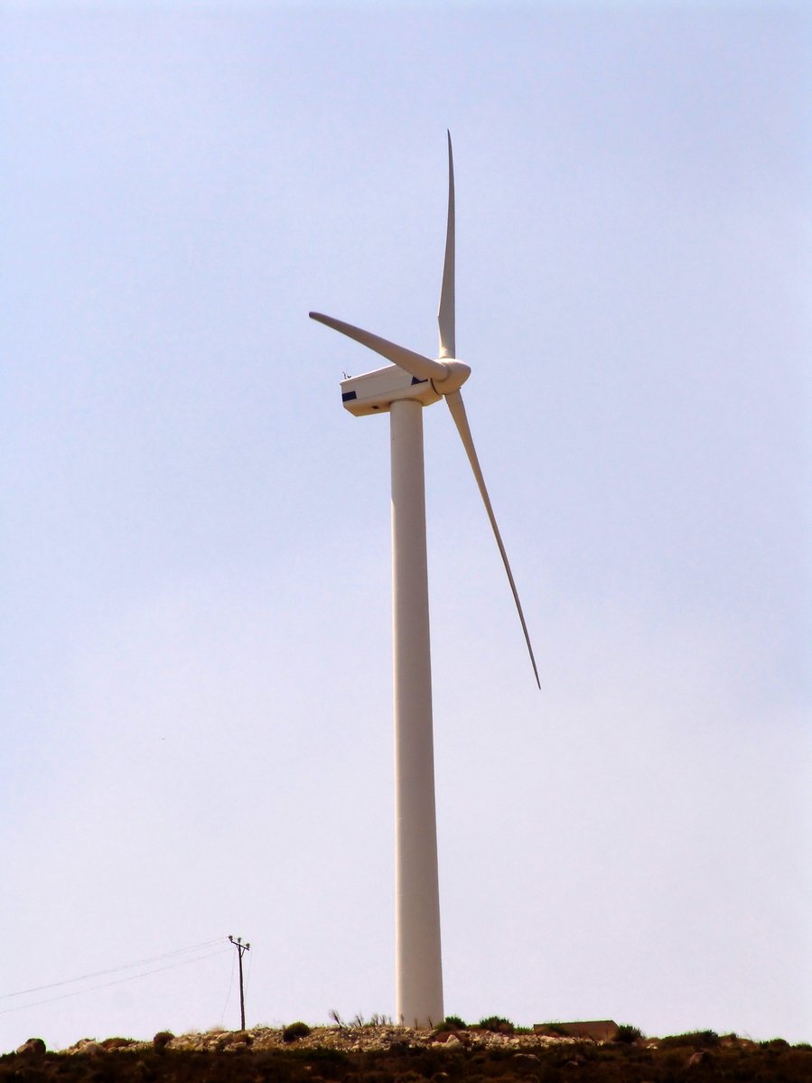 an airplane is flying in the air over a wind mill