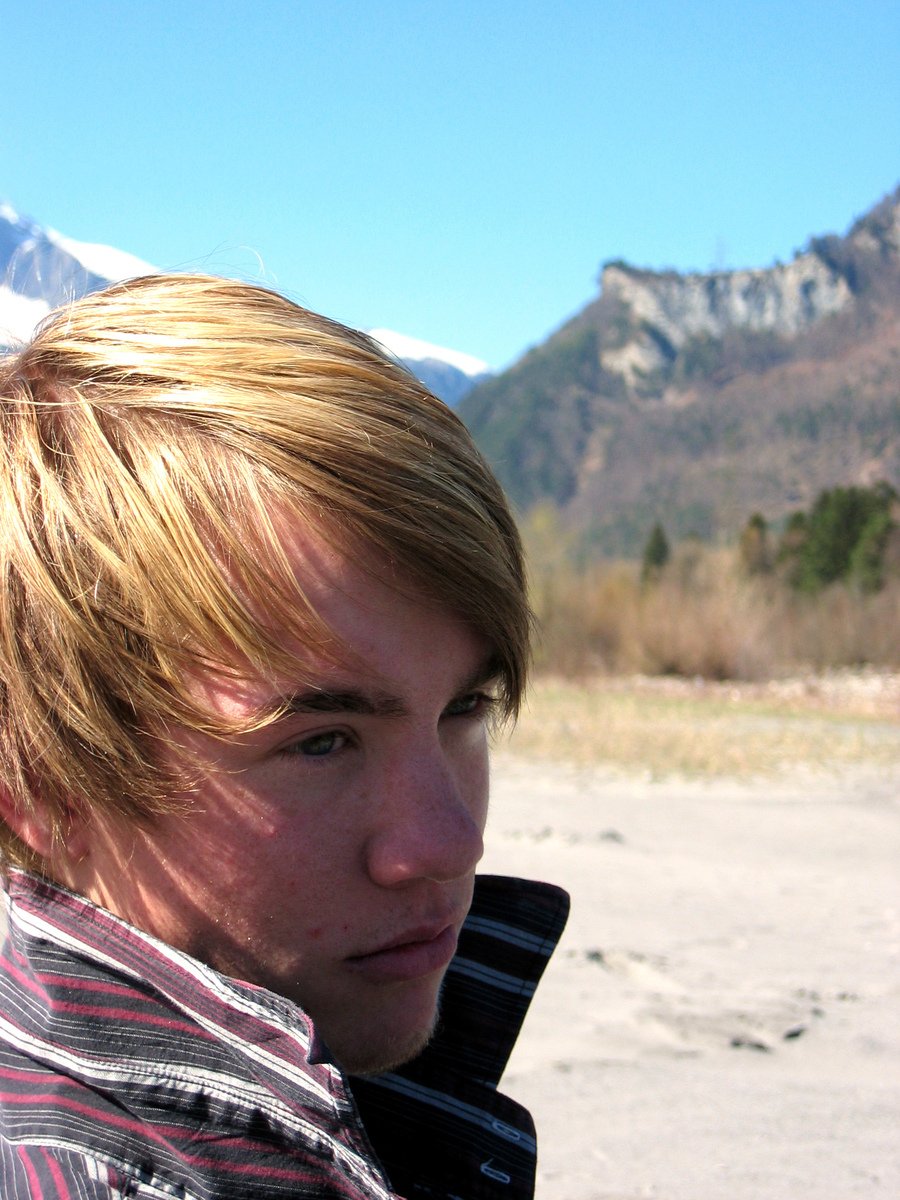 a close up of a young man with mountains in the background