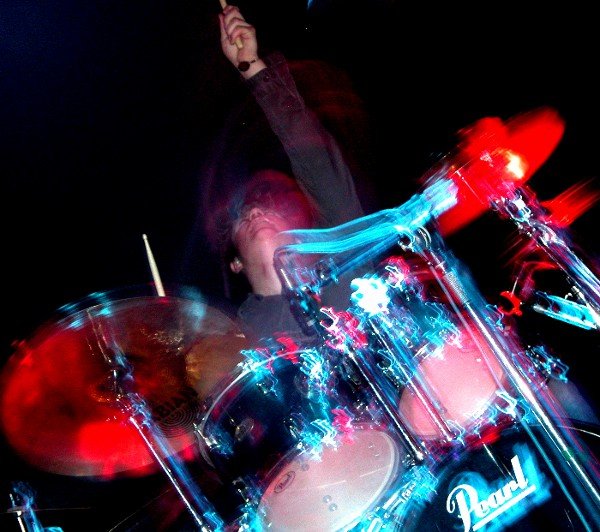 a drummer in a suit and a guitar, with drums and a microphone