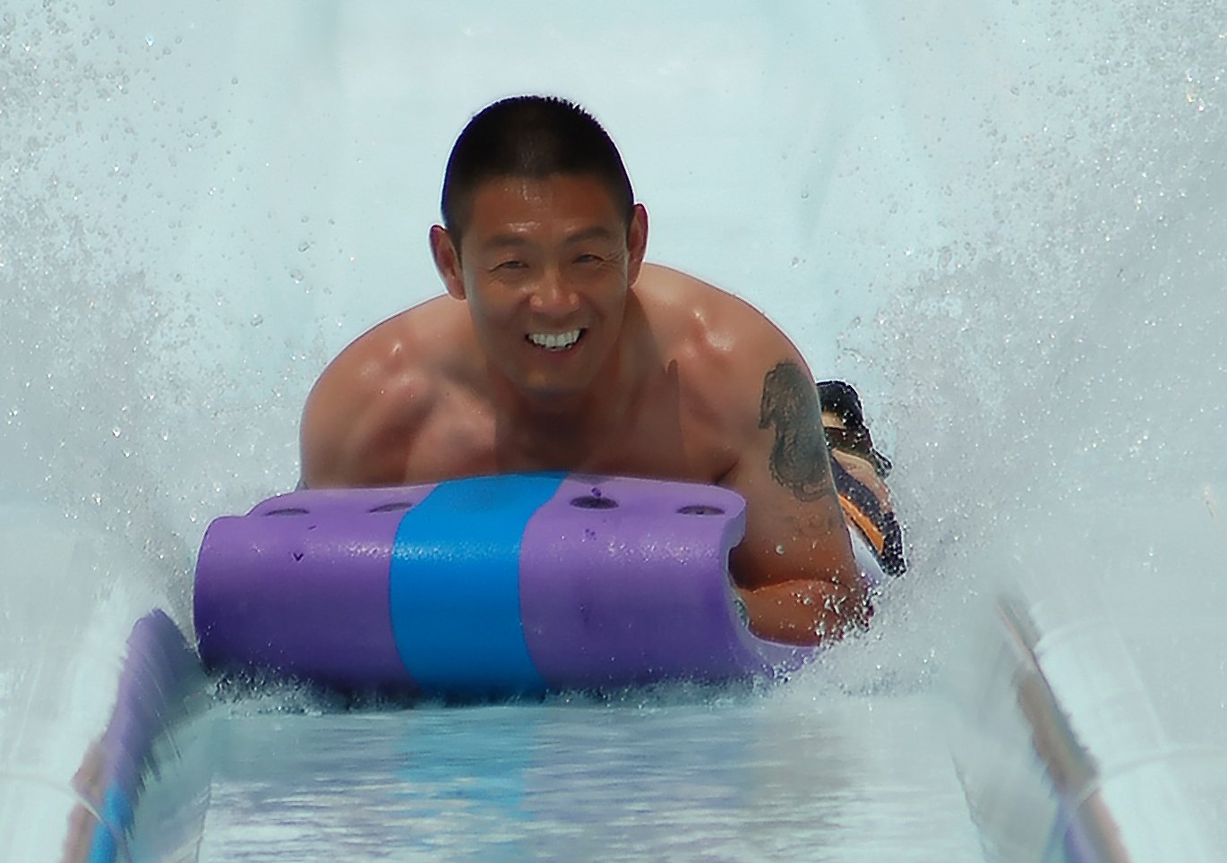 a guy rides a water slide in a swimming pool