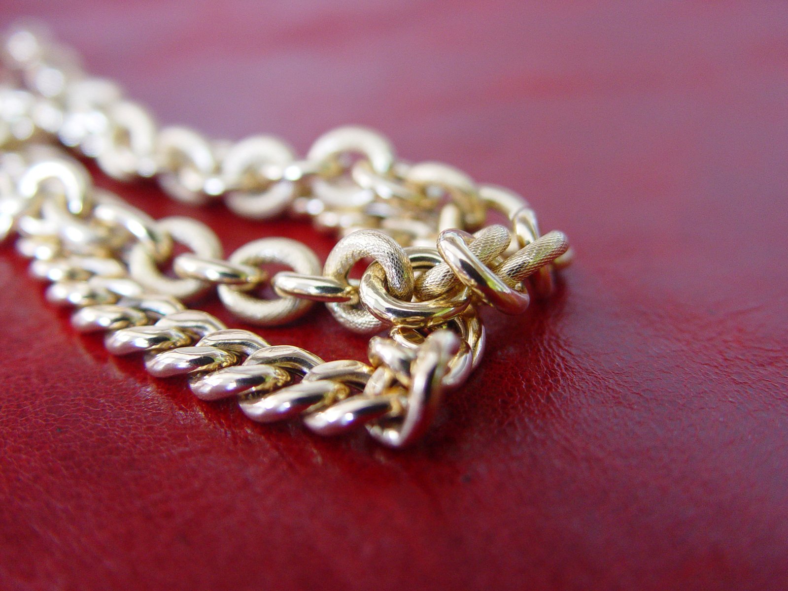 an 18k gold - filled link necklace sits on a red surface