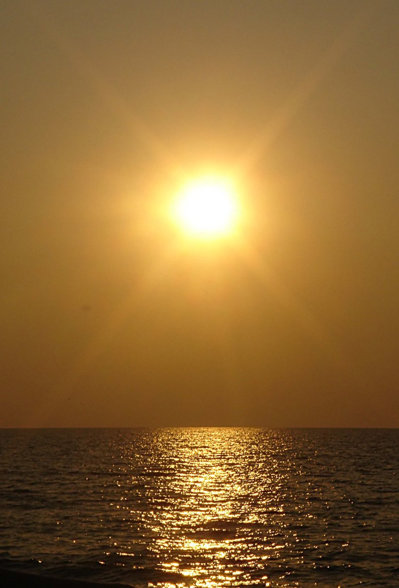 a bright sun reflecting off of the ocean in the evening